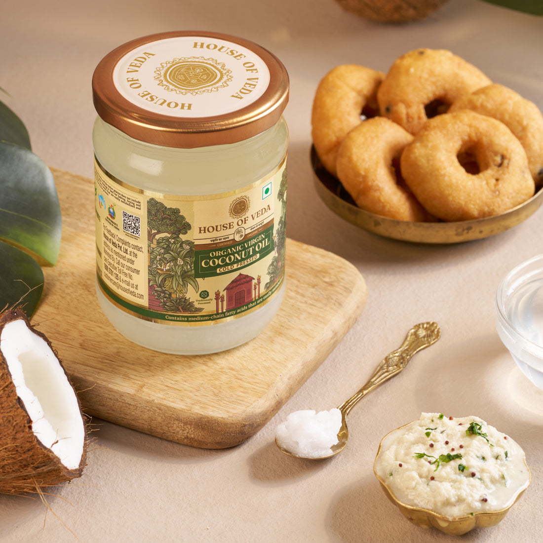 Jar of coconut oil from House of Veda with coconut and fried items on a table