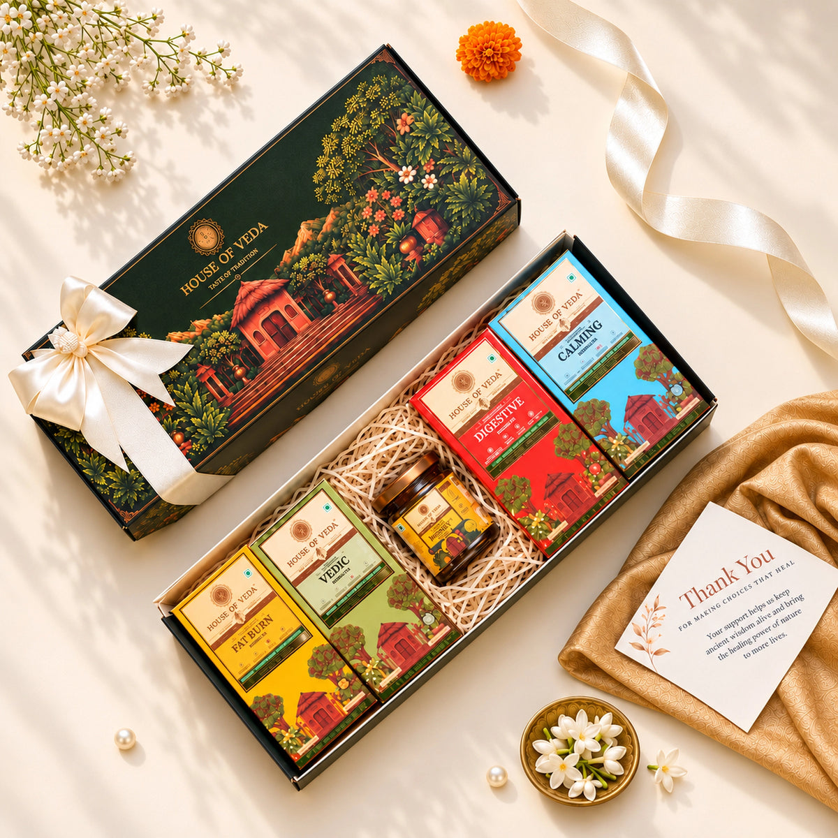 A styled flat-lay of a 'House of Veda' gift set featuring a dark forest green box with a white bow, alongside an open box filled with tea boxes, a honey jar, and a small card on a cream background with decorative flowers and a ribbon.